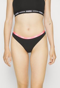 Crni pamučni bikini s ružičastim elastičnim pojasom na kojem se nalazi Puma logo. Glatka tekstura i uski dizajn. Bez dodatnih uzoraka ili akcenata.