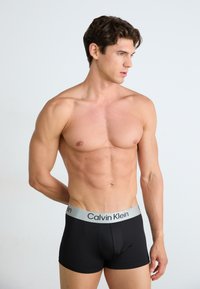 Boxer briefs negros con una cinturilla de logo plateada de Calvin Klein, diseño ajustado, textura suave y sin patrones ni acentos visibles.