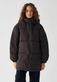 Tumši brūns pūšamais mētelis ar kapuci, ar rāvējslēdzēja priekšējo aizdari, elastīgajām aprocēm un teksturētu audumu ar quilted dizainu.