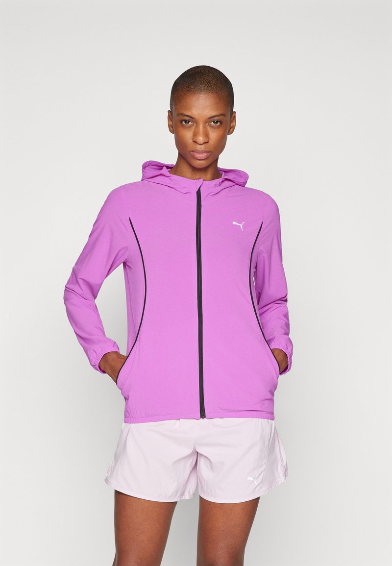Lätt lila zip-jacka med huva, med svarta detaljer och elastiska ärmslut, i kombination med rosa shorts. Slät struktur, atletisk passform.
