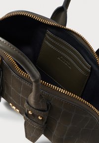 Ciemnozielona torba z fakturowanej powierzchni, złotym zamkiem błyskawicznym i podszewką. Posiada kieszonkę na karty wewnątrz oraz mocne uchwyty.