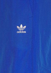 Blue fabric with a white Adidas Trefoil logo and text centered on the material.