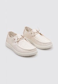 Zapatos de lona color beige claro con un upper texturizado, diseño de cordones y suela de goma blanca. El interior presenta un forro con patrón.