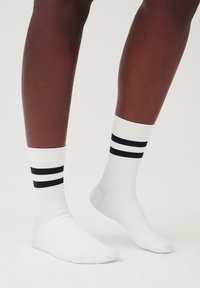 Weiße Sportsocken mit schwarzen Streifen oben, ausgestattet mit einer gerippten Textur und im Knöchellängen-Design. Geeignet für lässige Kleidung.
