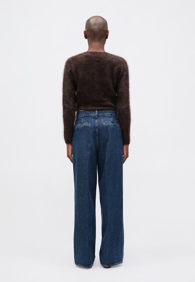 Suéter marrón de pelaje suave con mangas largas, combinado con jeans de pierna ancha azules. El conjunto presenta un ajuste relajado y una textura suave.