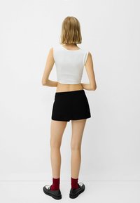 Vit kortärmad top utan ärmar med rundad halsringning, i sällskap med högmidjade svarta shorts och svarta skor med vita detaljer samt röda strumpor.