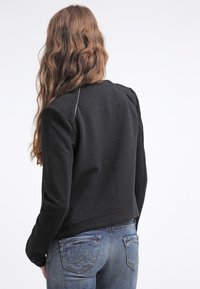 Černá textured bunda s cropped designem a čistými liniemi. Obsahuje kontrastní švy a kulatý výstřih. V kombinaci s modrými džíny.