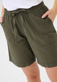 Shorts vert olive en tissu léger, avec une taille élastique et un cordon de serrage, deux poches frontales et une coupe décontractée.