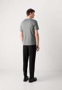 Tricou gri cu mânecă scurtă și guler rotund, asortat cu pantaloni negri texturați și pantofi negri, văzut din spate.