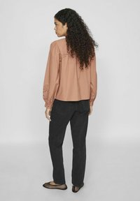 Blusa de color óxido con mangas largas, que presenta acentos bordados en los hombros. Combinada con jeans negros de pierna recta y zapatos planos de malla.