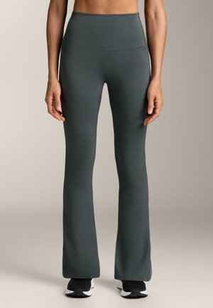 Pantalons de sport évasés taille haute en vert foncé, fabriqués à partir d'un tissu extensible. Présente une texture lisse et des détails de couture sur les côtés.