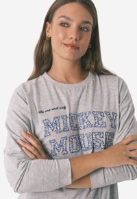 Grå langærmet t-shirt med "Mickey Mouse" i blå pyntet tekst med blomsterdesign. Løs pasform og rund halsudskæring.