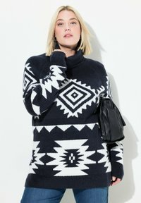 Maglione lavorato a maglia blu navy e bianco con motivi geometrici, colletto alto e maniche lunghe. Abbinato a una borsa nera con texture.