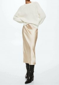 Chunky white knit sweater, beige satin midi skirt, and black knee-high boots. The outfit features soft textures and a layered silhouette.