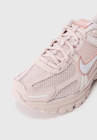 Scarpe da corsa Nike Vomero 5 di colore rosa chiaro, caratterizzate da tessuto in rete, linguetta imbottita, dettagli riflettenti e suola in gomma texturizzata con un motivo distintivo.