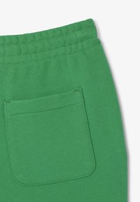 Gröna mjukisbyxor med en mjuk textur, med en elastisk midja och en enda bakficka. Tyget har en slät, enhetlig yta.