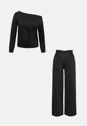 Zwart sweatshirt met lange mouwen en omgeslagen manchetten, gecombineerd met wijd uitlopende broek met hoge taille en elastische tailleband, op een witte achtergrond.