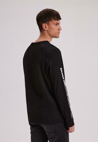 Czarna longsleeve z okrągłym dekoltem. Posiada białe napisy na prawej rękawie. Wykonana z miękkiego materiału o luźnym kroju.