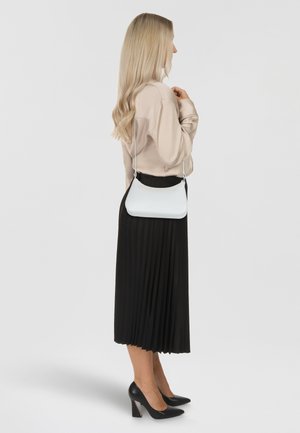 Borsa a tracolla bianca con superficie liscia e forma curvilinea, indossata con una blusa beige e una gonna plissettata nera, completata da tacchi neri.