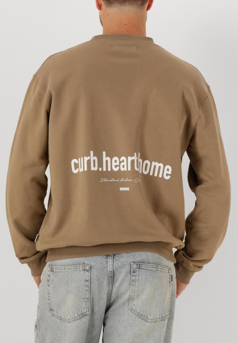 Brun sweatshirt med vit text "curb.hearthome" på baksidan, med ribbade cuffs och nederkant, tillsammans med ljusblå jeans.