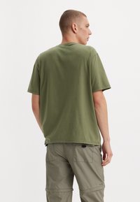 Olivovo zelené tričko s krátkym rukávom vyrobené z bavlny, s okrúhlym výstrihom a voľným strihom. Pohľad zozadu ukazuje jednoduchý dizajn bez vzorov alebo log. 