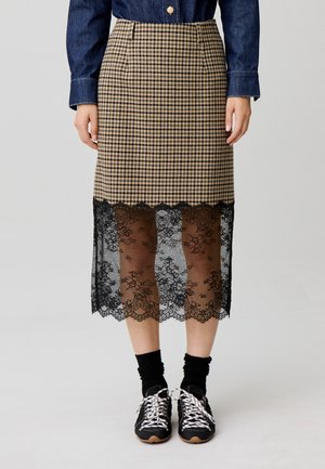 Falda desgastada con patrón de cuadros en tonos marrón claro y negro y encaje negro transparente que se extiende por debajo de la rodilla, combinada con calcetines negros y zapatillas.