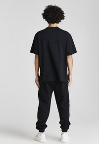 Svart bomullströja och matchande joggingbyxor med elastiska muddar. T-shirten har en avslappnad passform, medan joggingbyxorna har sidofickor. Vita sneakers är synliga.
