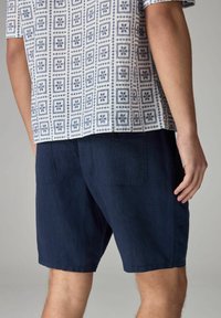 Marineblå shorts med en afslappet pasform, der har baglommer. Stoffet virker let og har en glat tekstur.