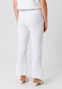 Witte gestructureerde flared broek met een rafelige rand, met een gladde afwerking bij de tailleband en subtiele details. Gedragen met witte hoge muiltjes.