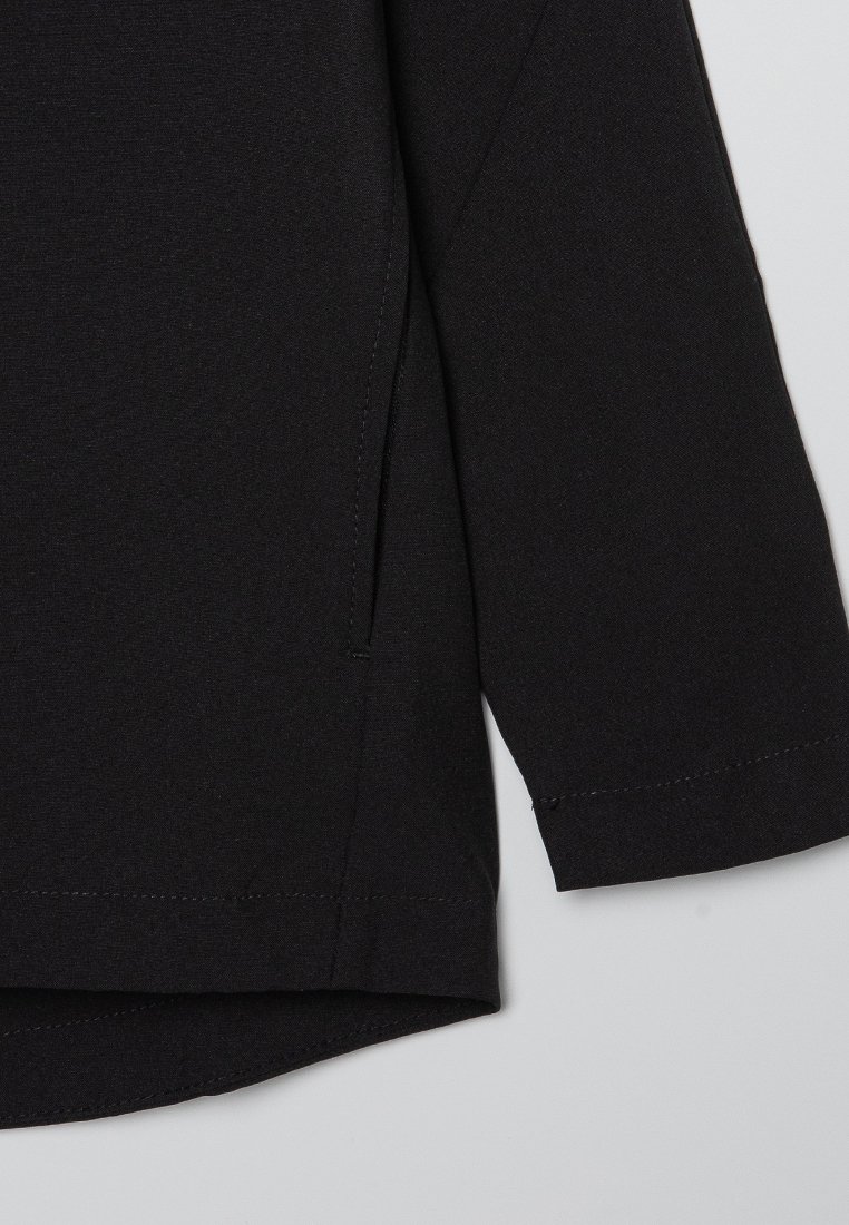 Indumento nero a maniche lunghe con scollo rotondo, caratterizzato da un orlo dritto e fessure sui lati. Tessuto liscio e senza modelli o accessori visibili.