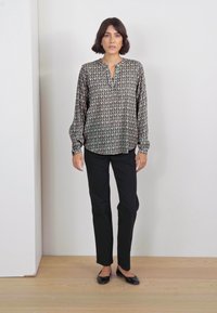 Blusa a fantasia con scollatura a V, maniche lunghe e polsini arricciati; abbinata a pantaloni neri skinny e scarpe basse nere.
