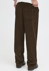 Pantaloni in velluto a costine marroni con design a gamba dritta, texture a coste e una tasca posteriore. La vita presenta una fascia elastica per il comfort.