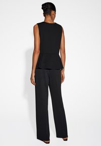 Zwart peplum top met een aansluitend lijfje en geplooide zoom, gecombineerd met zwarte wijde broek. Gladde textuur, minimalistisch ontwerp.