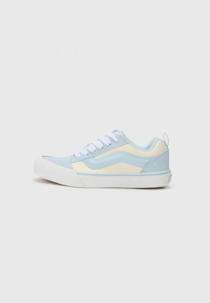 Lichtblauwe en crèmekleurige sneaker met een bovenwerk van suède en canvas, witte veters, rubberen zool en een trekloop aan de achterkant.
