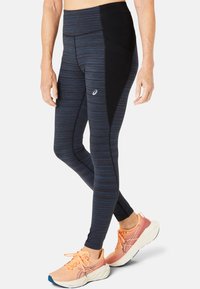 Granatowe legginsy z czarnym bocznym panelem, z teksturowanym prążkowanym wzorem i wysokim stanem. W zestawie z jasnoróżowymi butami sportowymi.