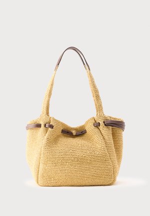 Vævet beige shopper med brun læderkant og knapdetalje, med to skulderstropper mod en lys baggrund.