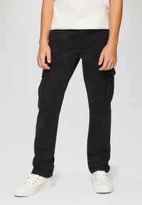 Schwarze Cargo-Hosen aus weichem Baumwollmaterial, mit Seitentaschen, geradem Bein und subtiler Textur, kombiniert mit weißen Sneakers.