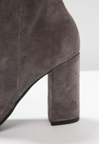 Bottine en daim gris avec un talon carré épais et une texture lisse, des coutures visibles le long du côté et un design à bout arrondi.