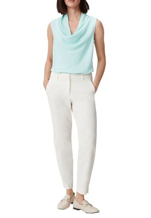 Haut bleu clair sans manches à col bénitier associé à un pantalon blanc fuselé ; le mannequin pose les mains dans les poches, portant des chaussures plates beiges.