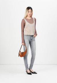 Béžová tílko s kulatým výstřihem, vrstvené přes hnědou dlouhý rukáv, spárované se světlými šedými skinny džíny a hnědou kabelkou s krokodýlí strukturou.