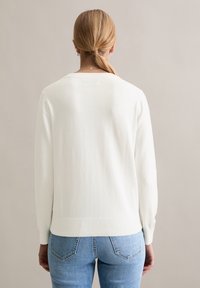 Witte gebreide trui met lange mouwen, ronde hals en geribbelde boorden. Gecombineerd met lichtblauwe denim jeans. Soepele textuur.