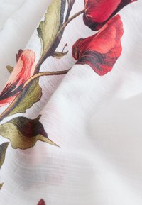 Material alb semitransparent cu un design imprimat de flori de mac roșii și frunze verzi, prezentând falduri moi și textură.