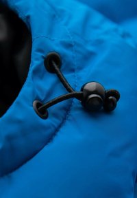 Kirkkaan sininen kangas, jossa on sileä pinta, musta säädettävä nyöri ja lukko hupun tai aukon sulkemiseen.