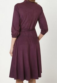 Lila, knielanges Kleid aus glattem Stoff, mit Kragen, Dreiviertelärmeln und einem gebundenen Taillengürtel sowie einem ausgestellten Saum.