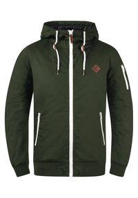 Giacca verde con cappuccio, dotata di zip frontale e dettagli bianchi. Presenta due tasche laterali e una tasca con zip sulla manica. Patch in pelle sul petto.