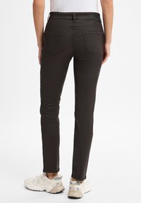 Donkerbruine slim fit jeans met een gladde textuur, voorzien van twee achterzakken en een gemerkte tailleband, gecombineerd met beige sneakers.