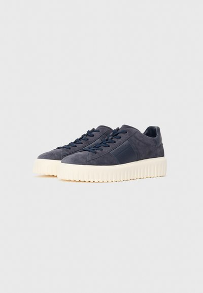 Pair of navy blue suede sneakers with thick white ribbed soles and matching navy laces on plain background.