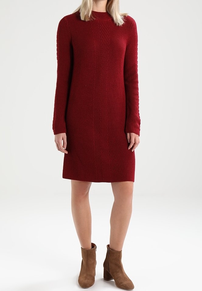 Rotes geripptes Strickkleid, lange Ärmel, schlanker Schnitt, Rundhalsausschnitt, knielang. Wird mit braunen Ankle Boots getragen, die Textur wirkt dick und gemütlich.
