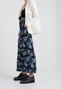 Svart croptop, vit blazer och marinblå blommiga vida byxor. Svarta platåskor med tjocka sulor. Släta texturer, livfulla bladmönster.