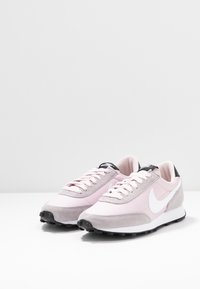 Ljusrosa löparskor med överdel i mocka och tyg, vit swoosh-logotyp, svarta häldekorationer och mönstrade gummisulor.